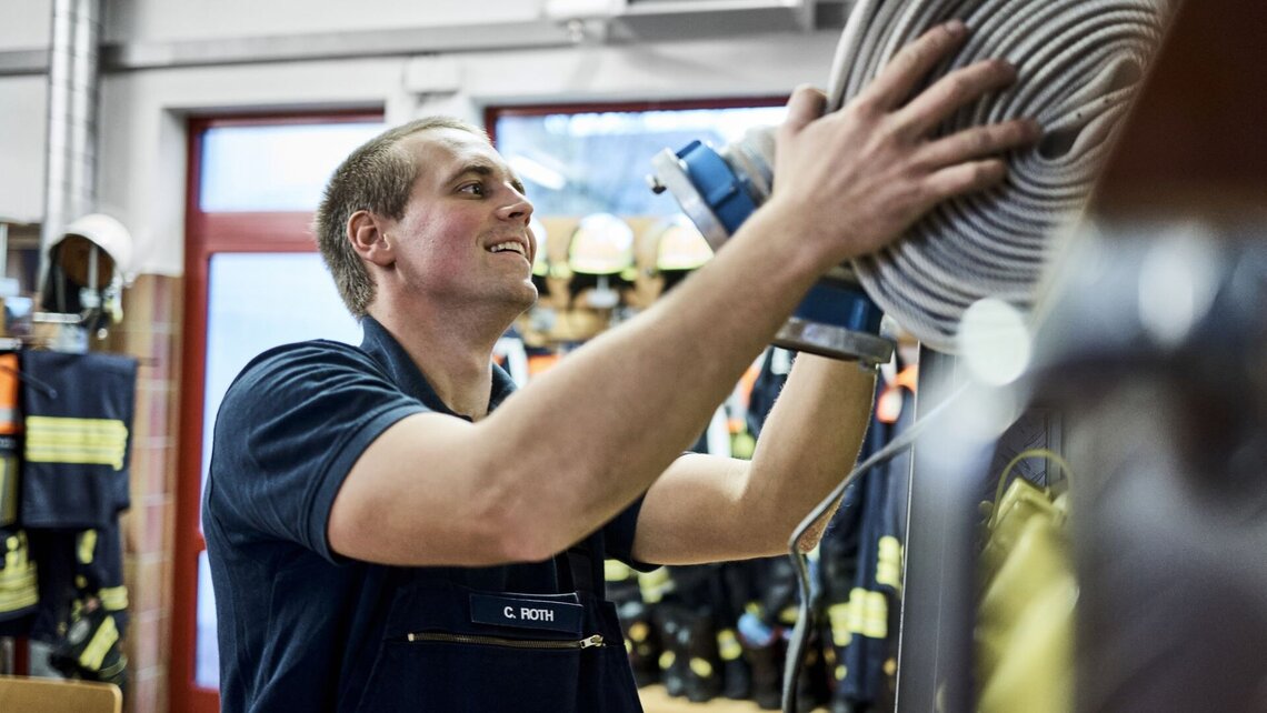 Feuerwehrmann Chris verstaut einen Feuerwehrschlauch.