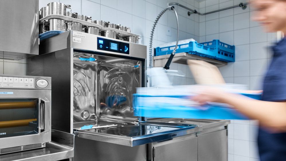 MEIKO Spülmaschine mit Wärmerückgewinnung in moderner Profiküche, Mitarbeiterin belädt die Maschine