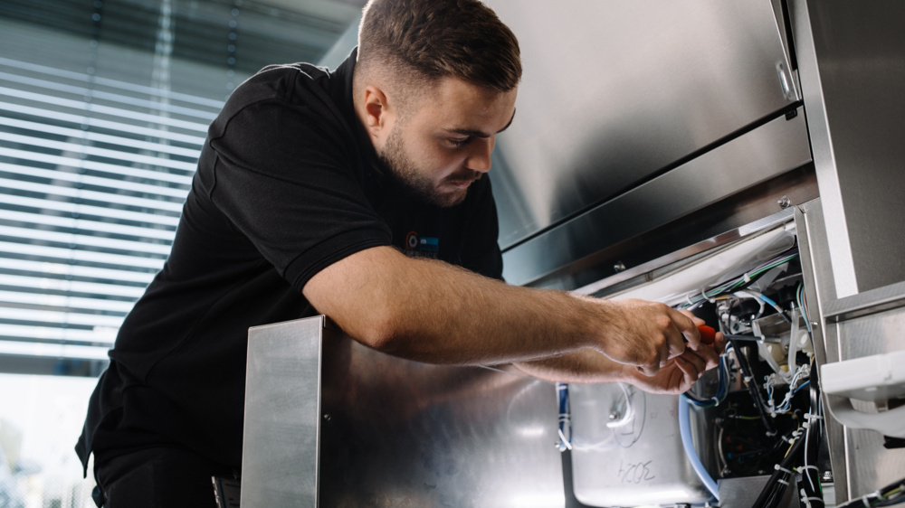 Technicen MEIKO réparant un lave vaisselle professionnel en cuisine 